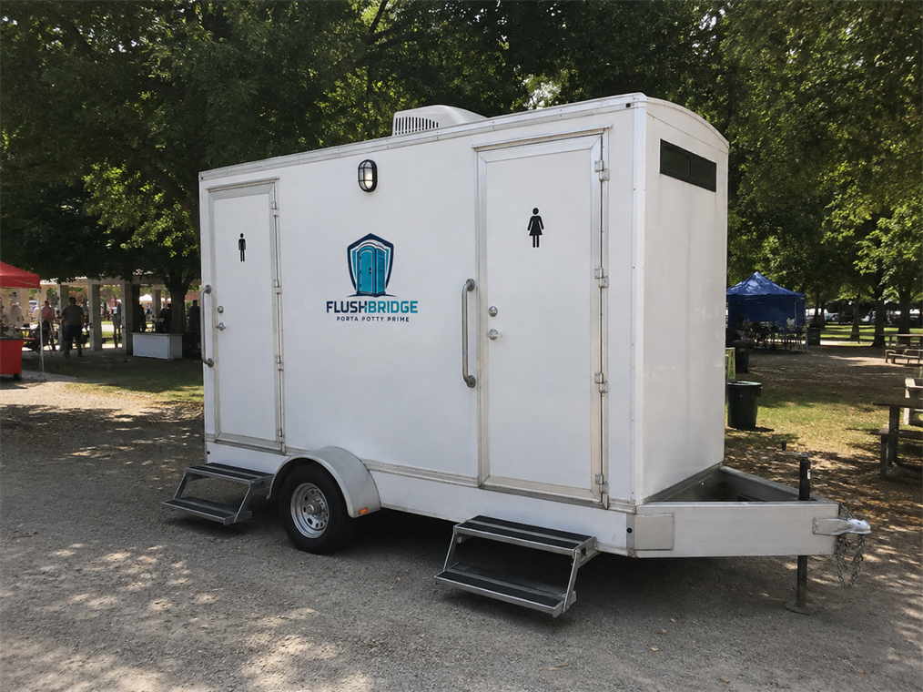 White multi-stall restroom trailer with entry steps parked on grass